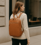 Woman walking with tan leather backpack, full-grain calfskin, minimalist style. Perfect for city commuting or travel.