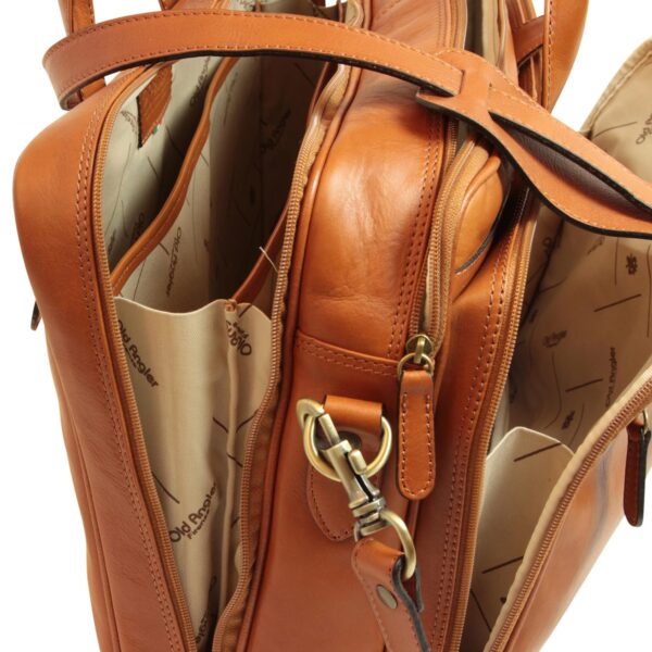 Internal view of a tan leather briefcase showing multiple zippered compartments, a brass swivel clasp for the shoulder strap, and a light-colored lining featuring the Old Angler logo.