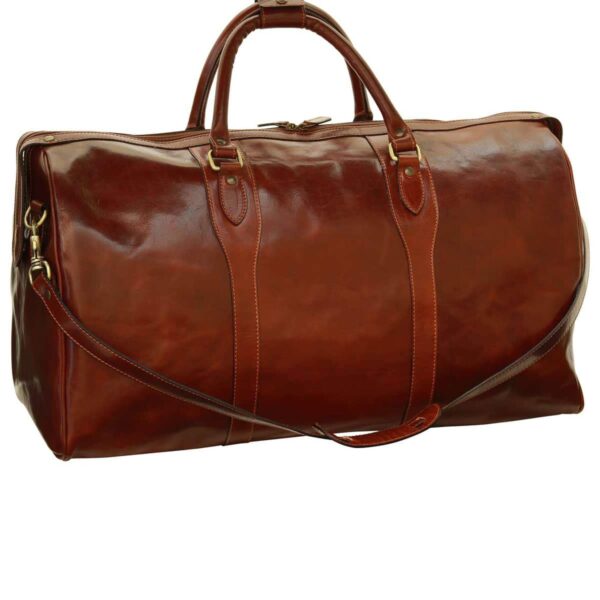 A large, **chestnut-brown leather duffel bag** with a glossy, polished finish. It features two rounded top handles with a leather connector, a detachable shoulder strap, and **antique brass-toned hardware**. The bag has a classic rectangular silhouette with vertical leather reinforcements extending from the handles.