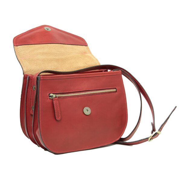 A vibrant red leather saddle bag shown with its flap open, revealing the natural tan suede lining and a horizontal zipper pocket on the front face of the main body. The bag features antique brass hardware, including a central magnetic snap and an adjustable crossbody strap with a buckle. The bag stands on its own, displaying its curved bottom and layered side construction.
