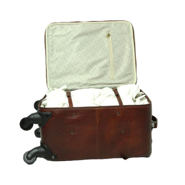 An open **brown leather carry-on suitcase** lying on its side, showing the interior. The inside features a patterned cream-colored lining, a zippered mesh pocket on the lid, and adjustable leather straps securing white packing paper in the main compartment. The four black spinner wheels are visible on the left side of the bag.
