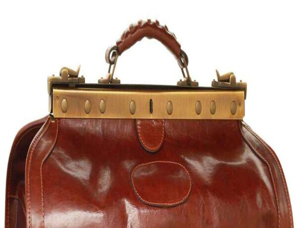Close-up view of a leather doctor bag featuring a brass frame closure, top handle with ergonomic grip, and vintage-style metal studs
