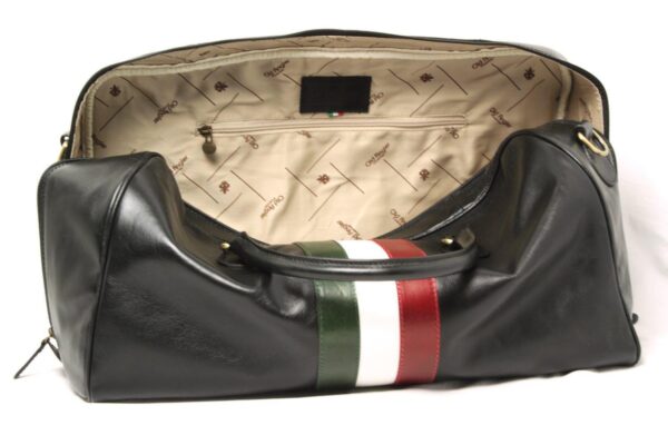 A wide-angle view looking into the open main compartment of the black leather duffel bag, showcasing the spacious interior lined with beige fabric patterned with the "Old Angler" logo and a horizontal zippered security pocket.