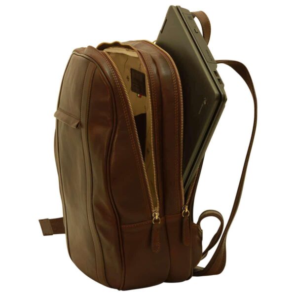 A side view of an open dark brown leather backpack showing its two main compartments. A laptop is being tucked into the rear padded section, while the front compartment reveals a patterned fabric lining and an internal brand leather patch.