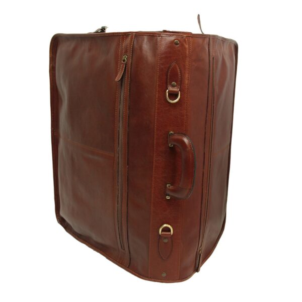 A side-angle view of a closed, high-quality **brown leather garment bag** standing upright against a white background. The image highlights a sturdy **leather handle**, brass-toned hardware (D-rings), and a vertical zippered pocket on the front.
