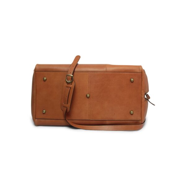The bottom view of a tan leather duffel bag on a white background, showing five brass metal feet for protection and a leather shoulder strap with a padded section resting across the base.