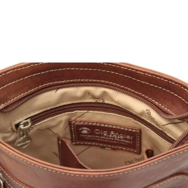 A close-up view of the interior of a brown leather bag, featuring a tan fabric lining patterned with the "Old Angler" logo. The interior includes a zippered pocket with a silver-tone pull and a stitched leather patch embossed with the brand name "Old Angler."