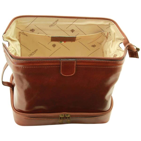 A front view of an open brown leather bag showing a spacious interior with "Old Angler Firenze" branded fabric lining, an internal slip pocket, and a separate zippered bottom compartment with dual brass pullers, isolated on a white background.