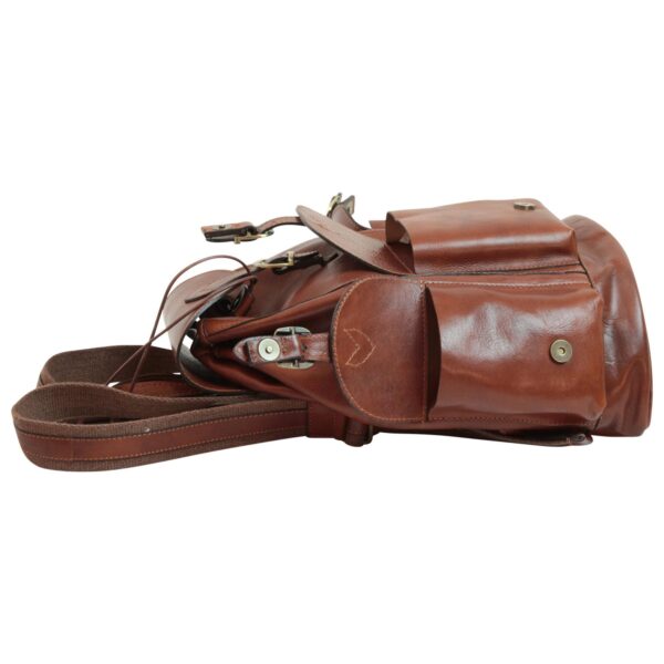 A side profile of a brown leather backpack lying flat on a white background, displaying multiple external pockets with magnetic snap closures, adjustable shoulder straps, and a drawstring top opening.