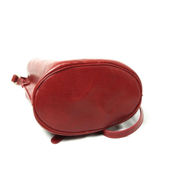 Bottom view of red leather shoulder bag showing oval base and smooth finish on white background