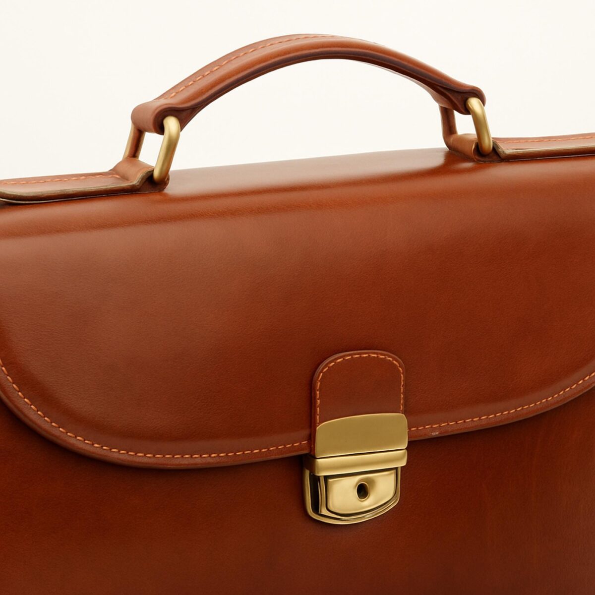 il_fullxfull.6888671775_4foo.jpg Close-up view of the top handle and brass tuck lock closure on a tan leather briefcase with detailed stitching
