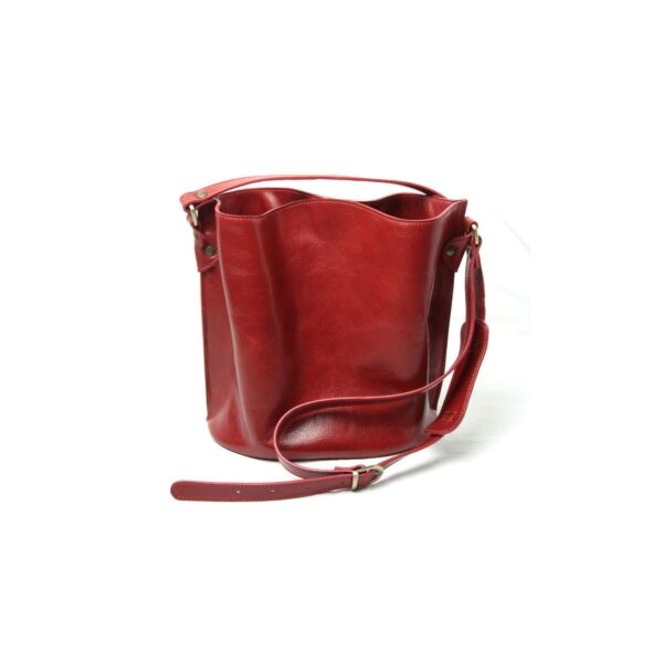 A studio shot of a red leather bucket bag on a white background, featuring a draped opening and an adjustable shoulder strap with brass hardware.