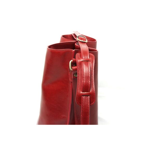 A side-view close-up of a red leather bag featuring an adjustable shoulder strap with a sliding padded section and a brass buckle, set against a white background.