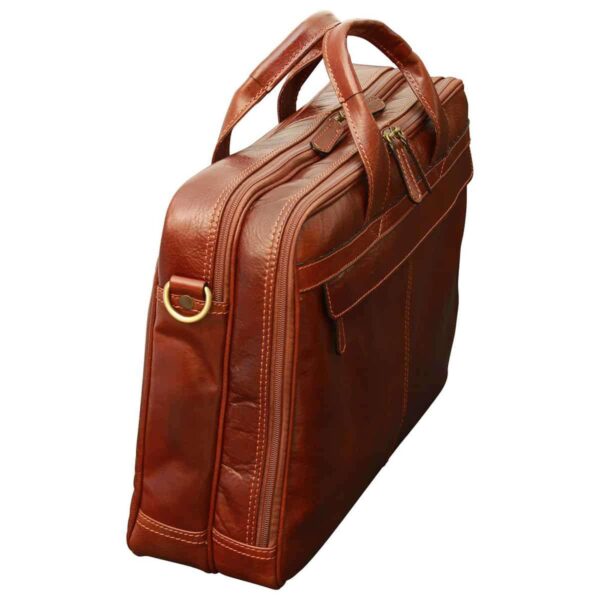 A side-angled view of a closed reddish-brown leather briefcase, featuring two main zippered compartments, sturdy rolled leather top handles, and brass-tone hardware for a shoulder strap attachment.