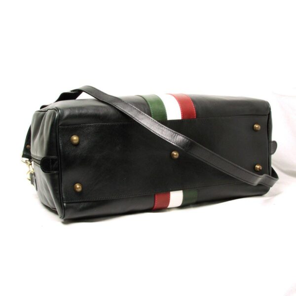 The bottom view of the black leather duffel bag, showing five brass protective feet (studs) designed to prevent wear and keep the leather off the ground, with the tri-color stripe visible wrapping around the edges.