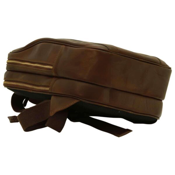 A top-down, side-profile view of the brown leather backpack lying flat. The shot emphasizes the two distinct zippered compartments, the smooth leather finish on the side panels, and the adjustable fabric-backed shoulder straps tucked underneath.