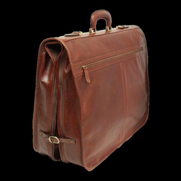A three-quarter side view of the **brown leather garment bag** in its folded, carry-on position. The image shows the bag's depth, a side **buckle strap** for secure closure, and the prominent **top handle**, set against a solid black background.