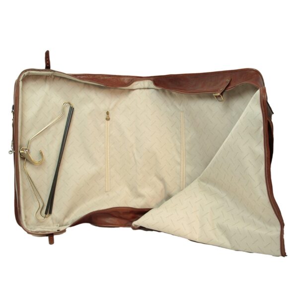 An open brown leather garment bag lying flat, revealing a cream-colored fabric interior with a subtle patterned lining, internal zippered compartments, and a metal clothes hanger tucked inside.