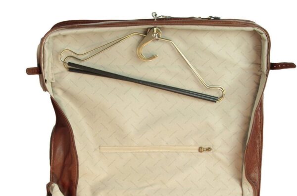 An open brown leather garment bag reveals a light-colored fabric interior with a built-in metal hanger and a zippered pocket at the bottom.