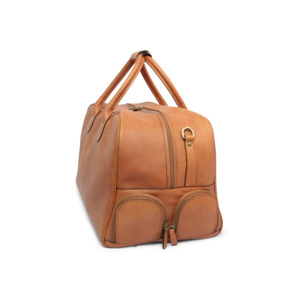 A side-angle view of a tan leather duffel bag on a white background, showing two small, rounded zippered pockets at the base of the side panel, a brass D-ring, and top handles joined by a leather connector.