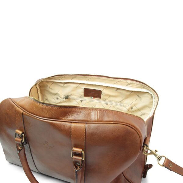 Open brown leather duffle bag by Old Angler showing a spacious cream branded interior lining, an Italian-made label, gold-tone hardware and zipper, with shoulder strap attached, on a white background