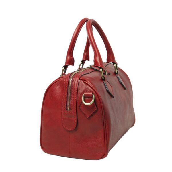 A side view of a red leather satchel-style handbag on a white background, featuring rounded top handles, a brass zipper closure, and a D-ring on the side for attaching a shoulder strap.