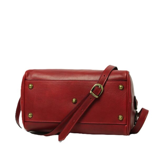 A view of the bottom and side of a red leather handbag, featuring five brass protective studs (feet) on the base and an adjustable leather shoulder strap with a brass buckle, set against a white background.