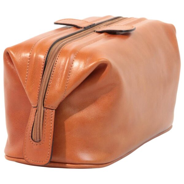 Side-angled view of a closed tan leather toiletry bag, featuring a central zipper that extends down the sides, leather pull tabs, and a structured rectangular silhouette with a smooth finish.