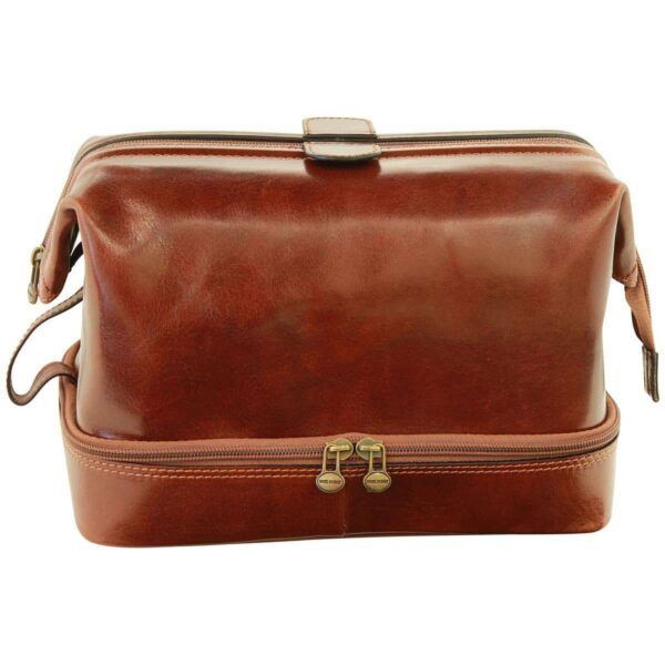 A front-facing view of a closed, brown polished leather toiletry bag featuring a classic "doctor bag" framed top and a separate zippered bottom compartment. The bag is equipped with antique-style brass hardware and double zippers on the base, showcasing its rich texture and structured design.