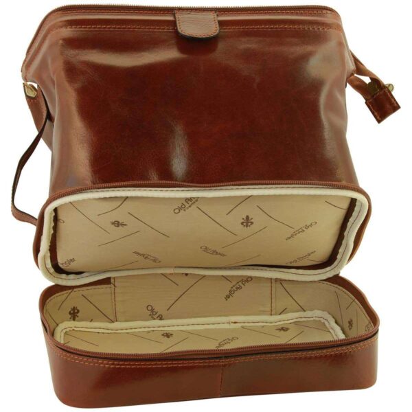 An open view of a brown leather toiletry bag, specifically highlighting the zippered bottom compartment. The interior is lined with a cream-colored fabric featuring the "Old Angler Firenze" logo and fleur-de-lis motifs, matching the structured "doctor bag" design of the upper section.