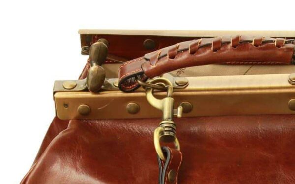 A close-up shot of an open vintage-style brown leather doctor's bag, showing the interior lining, the brass-toned metal frame with rivets, and a detachable shoulder strap connected by a swivel lobster clasp.