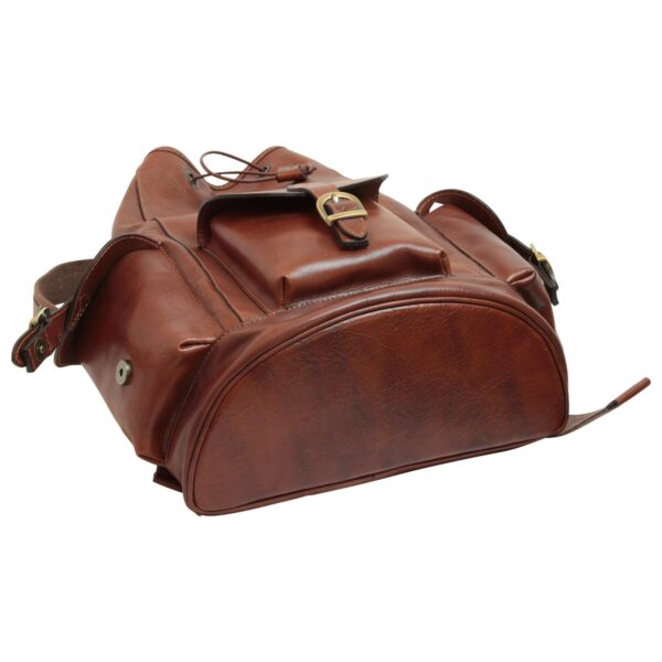 A low-angle view of a brown leather backpack resting on its side against a white background, highlighting its reinforced semi-circular base, a front pocket with a brass buckle closure, and a drawstring top.