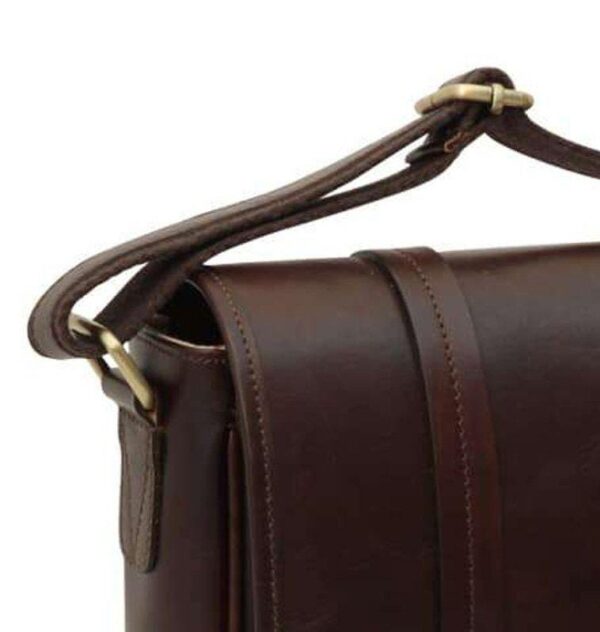 A close-up view of the upper corner of the dark brown leather messenger bag, highlighting the adjustable shoulder strap with its brass buckle and the clean, precise stitching along the edge of the top flap.