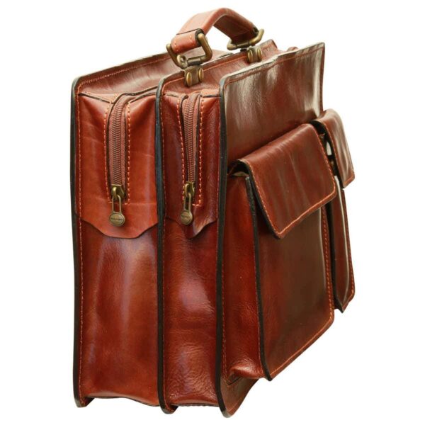 A three-quarter side view of a cognac-colored leather briefcase, highlighting its dual zippered main compartments, brass-tone hardware, and the profile of two front utility pockets with flap closures.