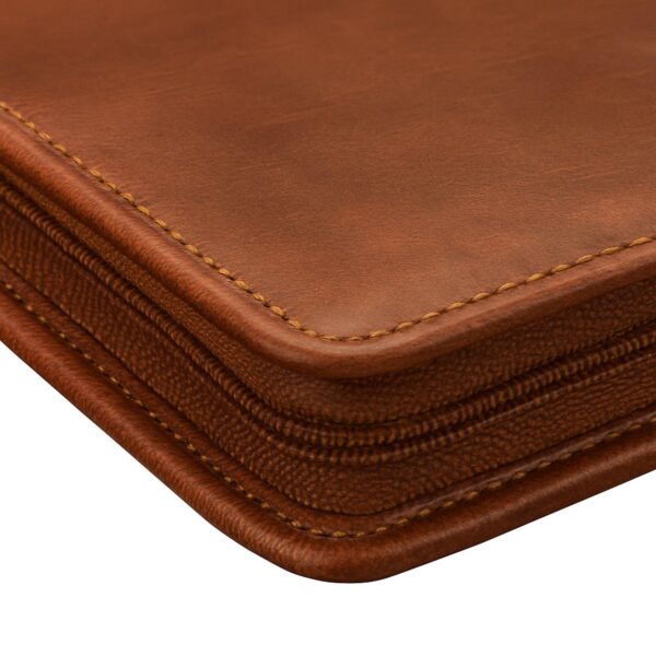 A detailed close-up of the corner of a brown leather portfolio, highlighting the high-quality grain and texture of the material. The image showcases precise, contrast stitching along the rounded edges and a sturdy, matching zipper track that wraps around the side.